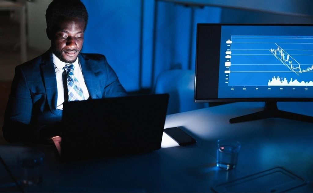 Compliance analyst reviewing KYC transaction data on dual screens at night