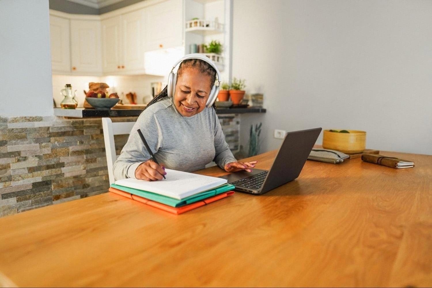 Woman with headphones taking notes at home while joining an online lesson on a laptop